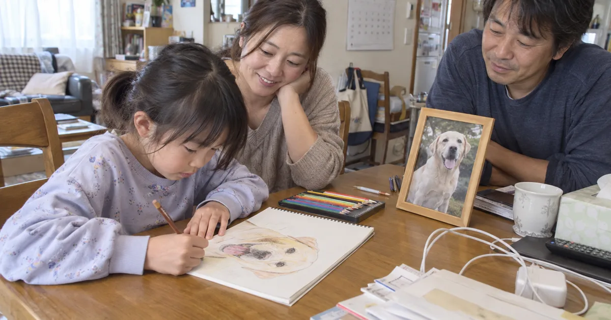 ラブラドールレトリバーの絵を描く子どもと見守る40代の夫婦